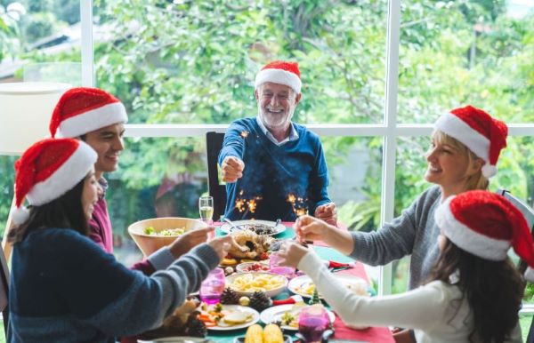 A group of people wearing Christmas hats are sitting at a table that is covered in plates of food.